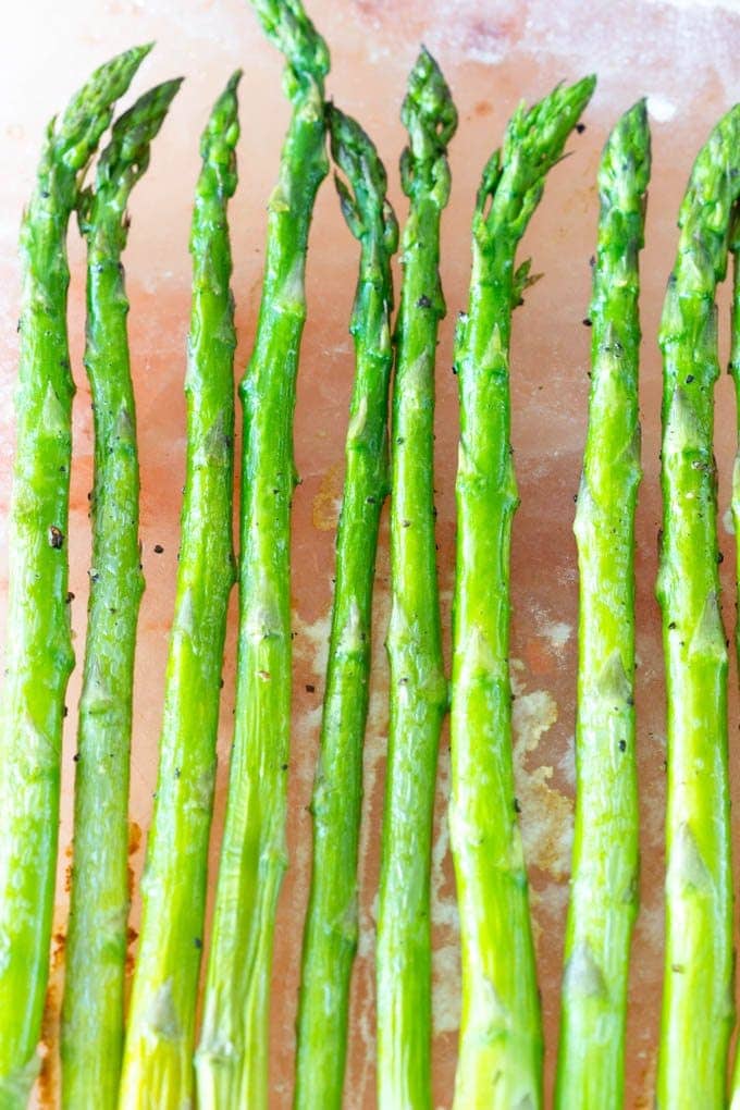 Spears of asparagus cooking on a pink Himalayan Salt Block