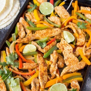 seasoned cooked chicken pieces with sliced red and yellow bell peppers on sheet pan