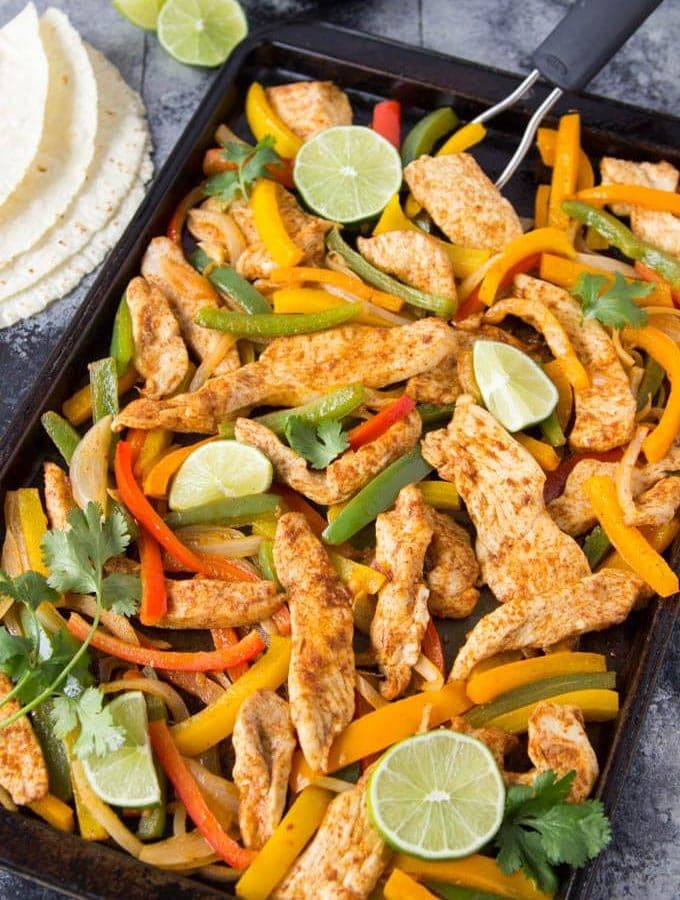 seasoned cooked chicken pieces with sliced red and yellow bell peppers on sheet pan