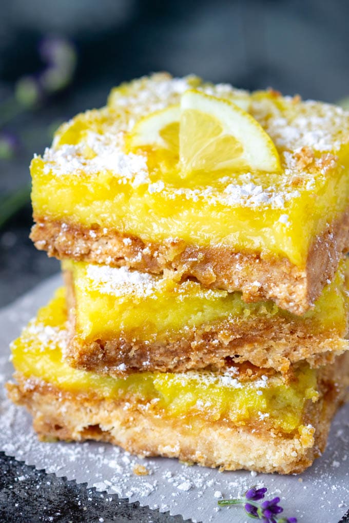 Three lemon bars stacked up on top of one another and dusted with powdered sugar