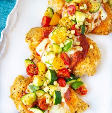 chicken Parmesan topped with fresh tomatoes, zucchini and corn on a white platter