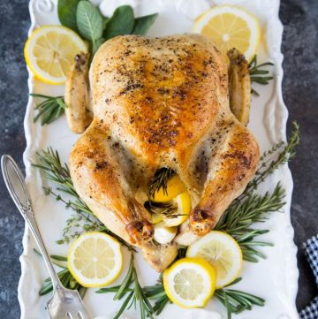 Whole Roasted Chicken with Lemon, Garlic and Rosemary on white serving platter