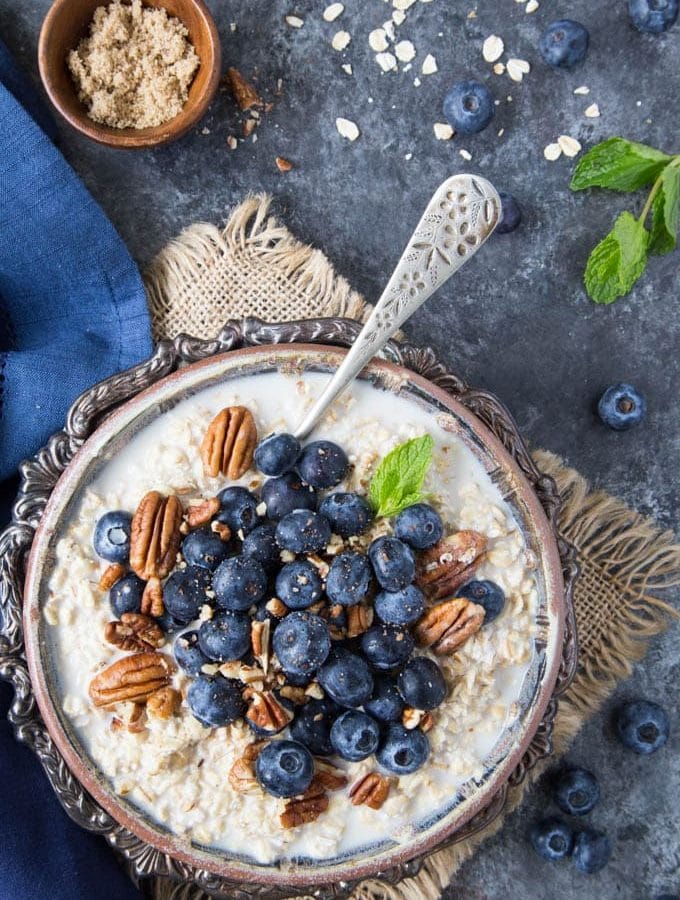 Oatmeal in a fancy silver bowl topped with fresh blueberries and chopped pecans