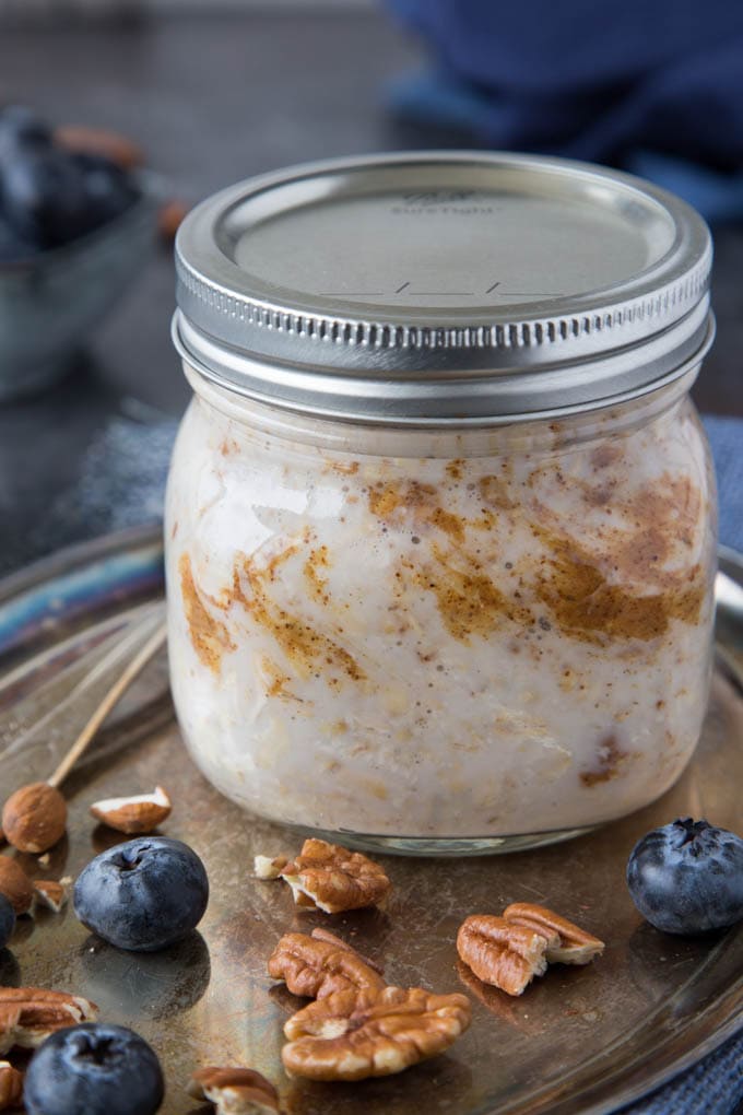 mason jar with overnight oat ingredients (oats, almond butter, almond milk and Greek yogurt) stirred together. The metal lid has been placed on the mason jar and it is now ready to be placed in the refrigerator overnight. been 