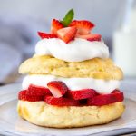 golden brown shortcake sliced in half and layered with slice strawberries and whipped cream.